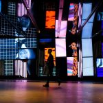 Une femme traverse une salle avec de nombreux écrans colorés lors d'une visite guidée.
