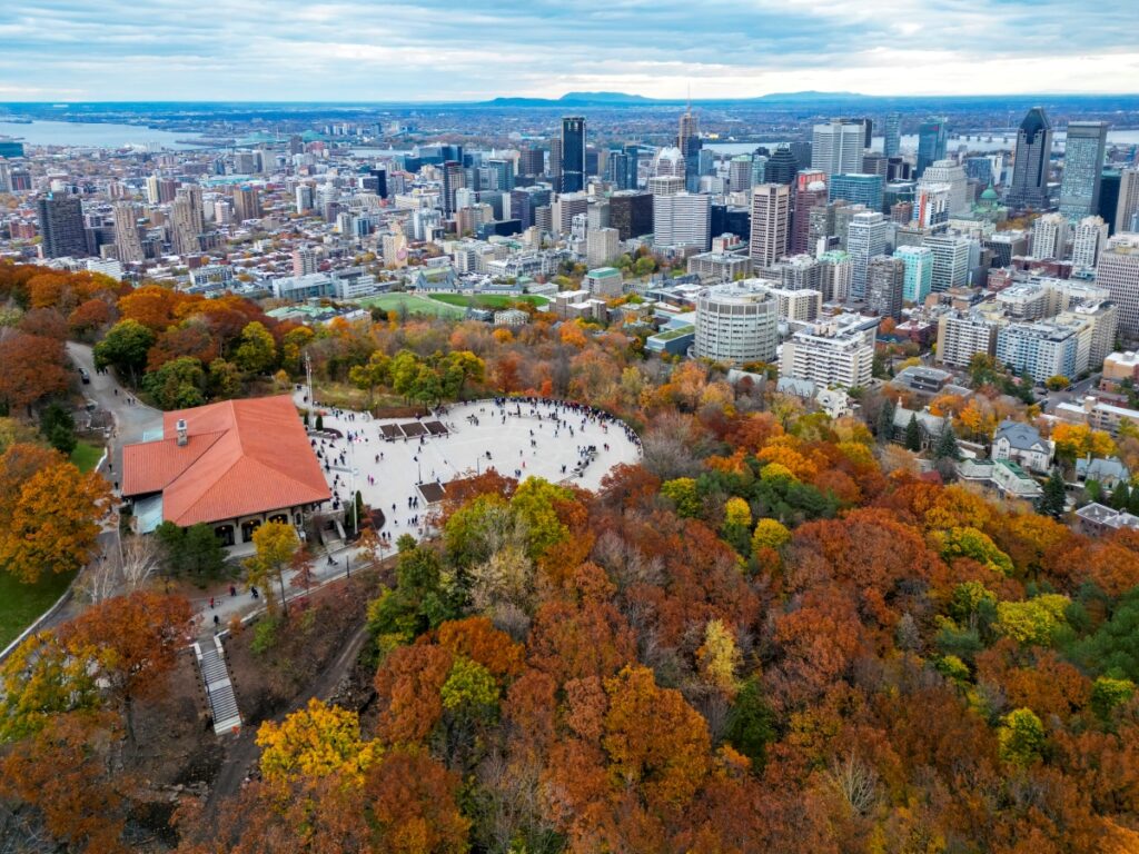 Aerial view of Mount Royal’s Kondiaronk Belvedere with crowds enjoying fall foliage, set against the backdrop of downtown Montreal’s skyline.