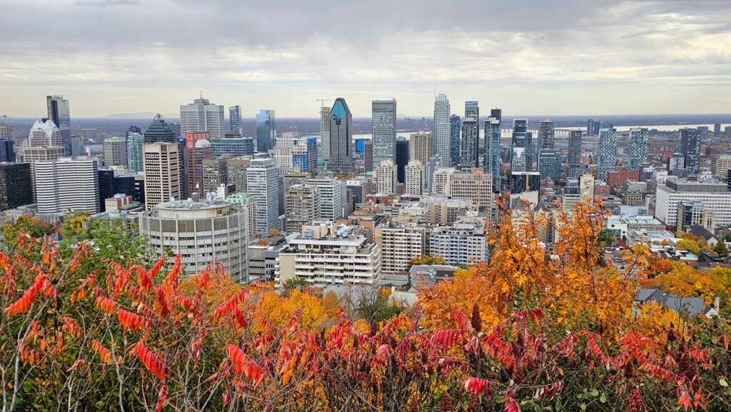 Panoramic fall view of downtown Montreal from Kondiaronk Belvedere on Mount Royal, framed by vibrant red and orange foliage.