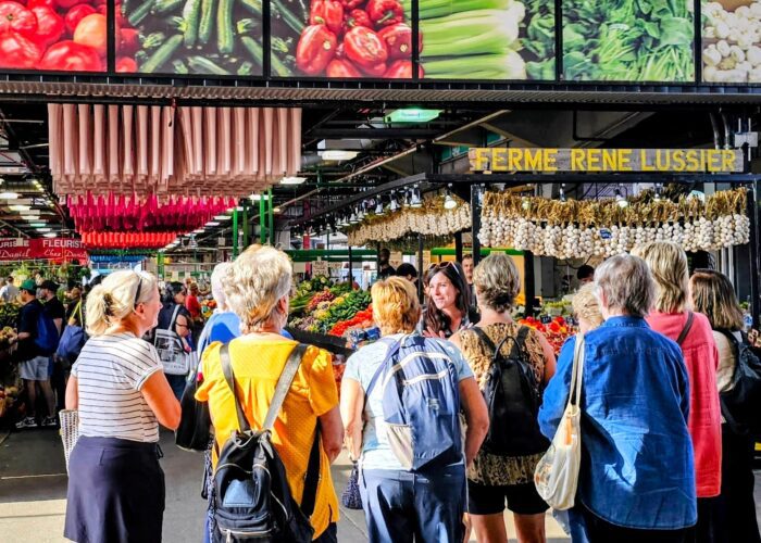 Un guide de MTL Detours s'adresse à un petit groupe de visiteurs lors d'une visite guidée à pied à l'intérieur du marché Jean-Talon, à Montréal.