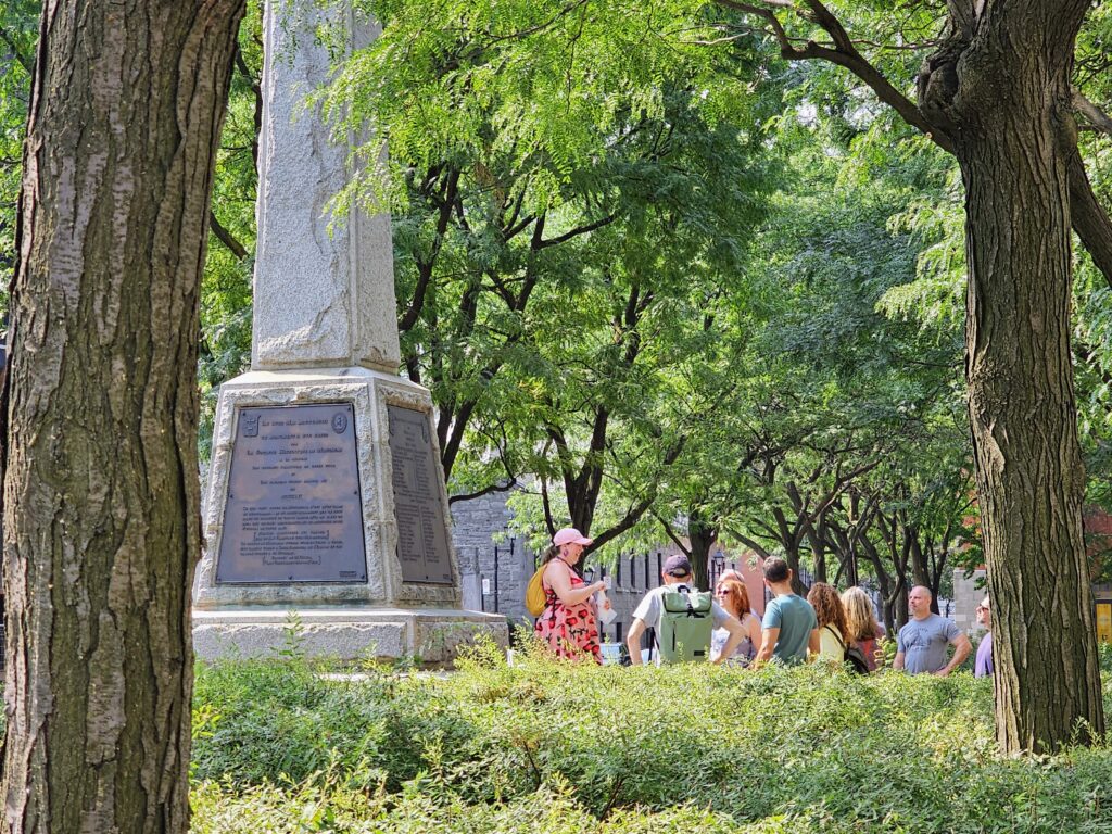 MTL Detours guide leading a small walking tour group near a monument in Old Montréal.